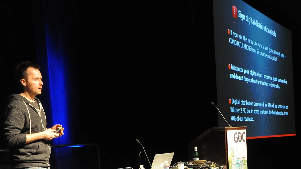 Marcin Iwiński na scenie GDC 2012 przy slajdzie o sprzedaży cyfrowej Wiedźmina 2